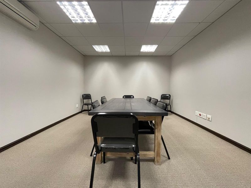 A functional office meeting room featuring a suspended ceiling, recessed lighting, wall-mounted air conditioning, and neutral carpeted flooring.