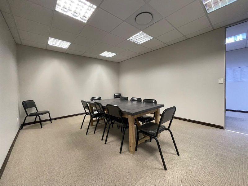 A functional office meeting room featuring a suspended ceiling with recessed lighting and neutral carpet flooring, suitable for professional use.