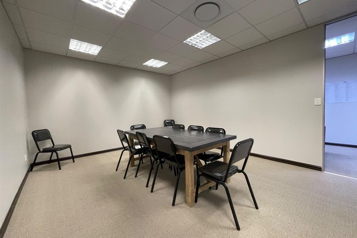 A functional office meeting room featuring a suspended ceiling with recessed lighting and neutral carpet flooring, suitable for professional use.