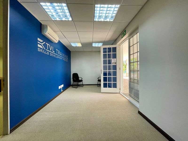 A bright, open-plan office space featuring a suspended ceiling, recessed lighting, split-system air conditioning, and direct access to an outdoor area via a french door.