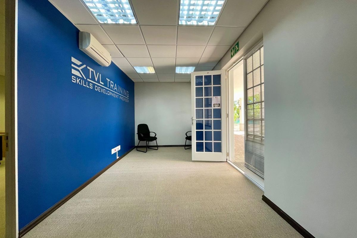 A bright, open-plan office space featuring a suspended ceiling, recessed lighting, split-system air conditioning, and direct access to an outdoor area via a french door.