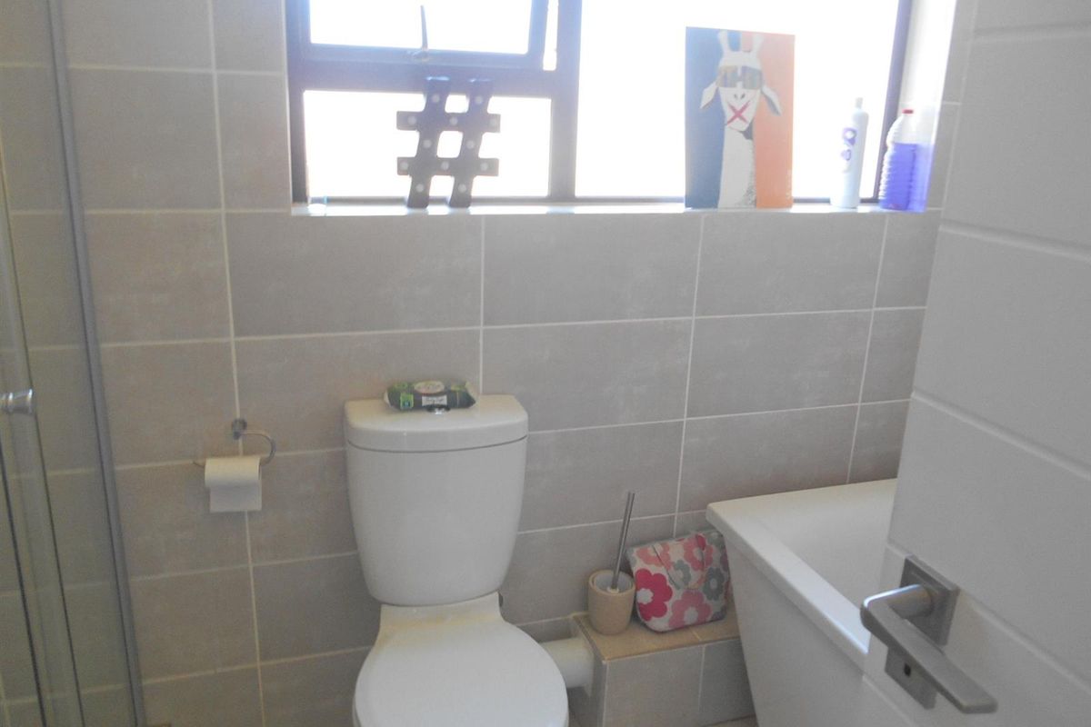A functional bathroom featuring a toilet, bathtub, and shower enclosure with neutral wall and floor tiling.