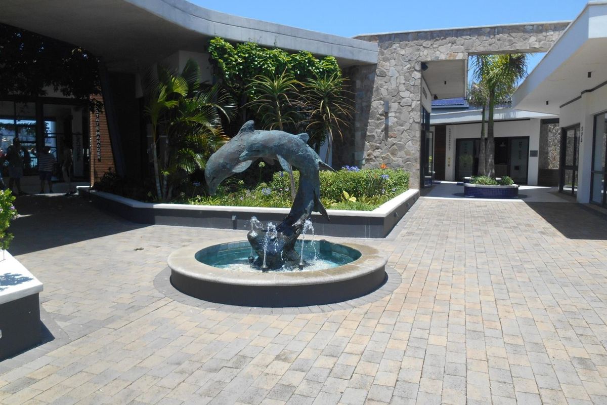 A well-maintained paved courtyard featuring a central dolphin water fountain, stone-clad walls, and landscaped garden beds within a modern apartment complex.