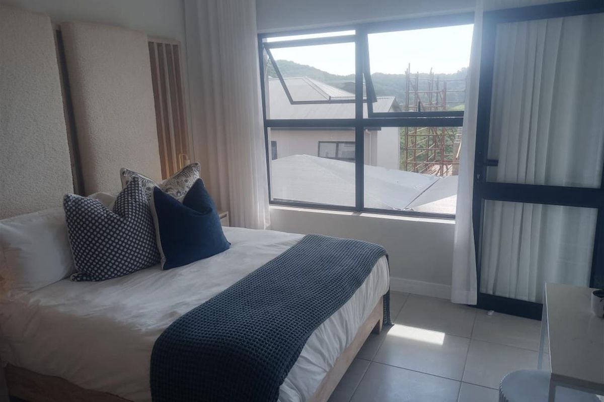 A well-lit bedroom featuring neutral tiled flooring, modern aluminium window and door frames, and a clean, contemporary aesthetic.