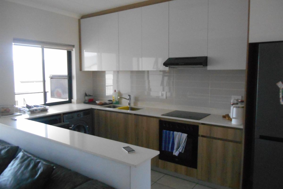 Modern kitchen featuring sleek white and wood-tone cabinetry, stone countertops, integrated appliances, and a functional breakfast bar overlooking the living area.