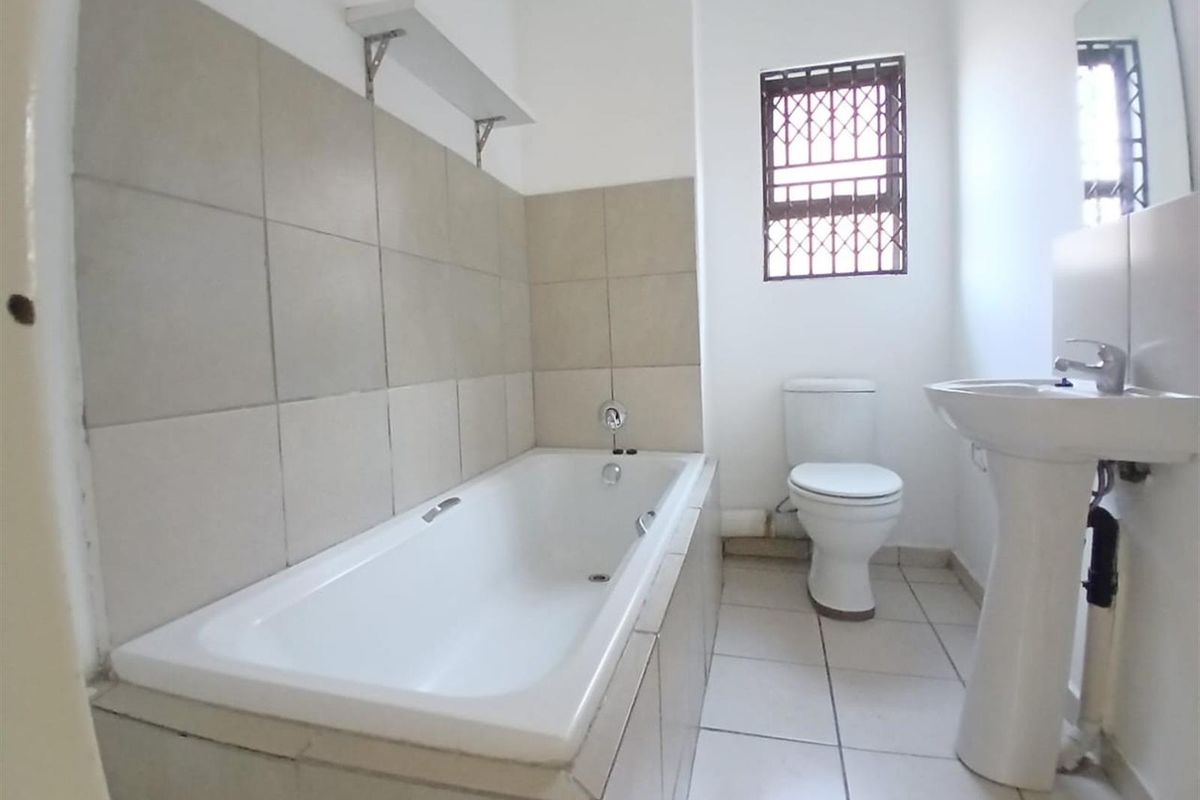 A functional bathroom featuring a built-in bathtub with tiled surround, a pedestal basin, and a toilet, finished with neutral floor tiles.