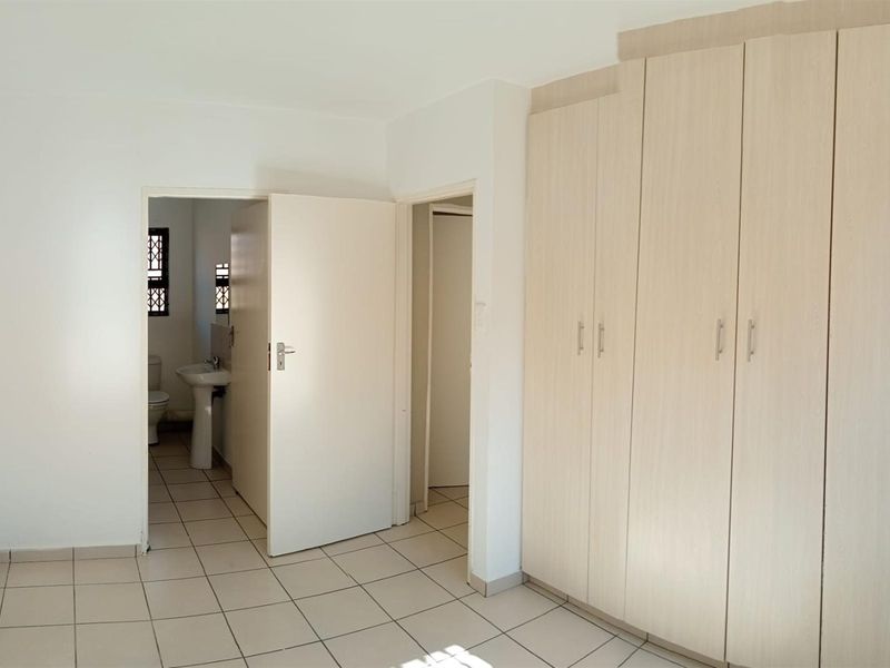 A bright, empty bedroom featuring neutral tiled flooring and ample built-in cupboard storage, with direct access to an en-suite bathroom.
