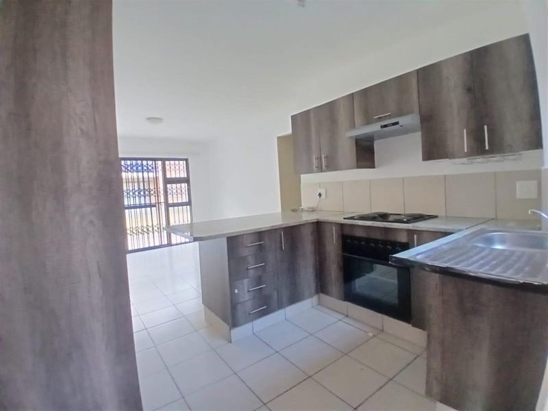 Open-plan kitchen featuring modern wood-finish cabinetry, built-in oven, gas hob, and tiled flooring, flowing into a bright living area with security gate access.