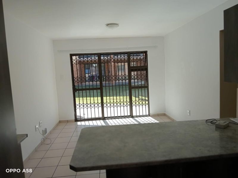 An open-plan living area featuring tiled flooring, a breakfast counter, and a sliding door with a security gate leading to the exterior.