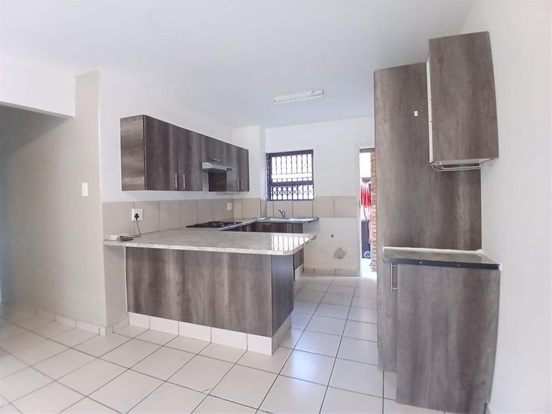 A clean, empty kitchen featuring modern wood-look cabinetry, stone-effect countertops, a built-in hob with extractor, and neutral floor tiles.