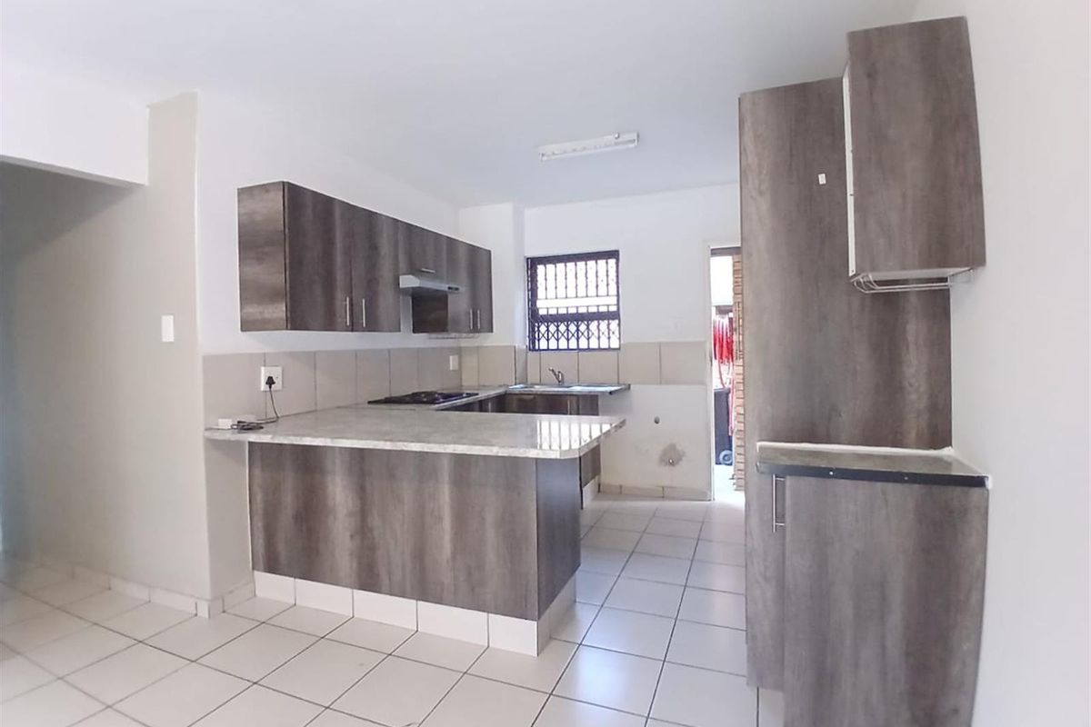 A clean, empty kitchen featuring modern wood-look cabinetry, stone-effect countertops, a built-in hob with extractor, and neutral floor tiles.