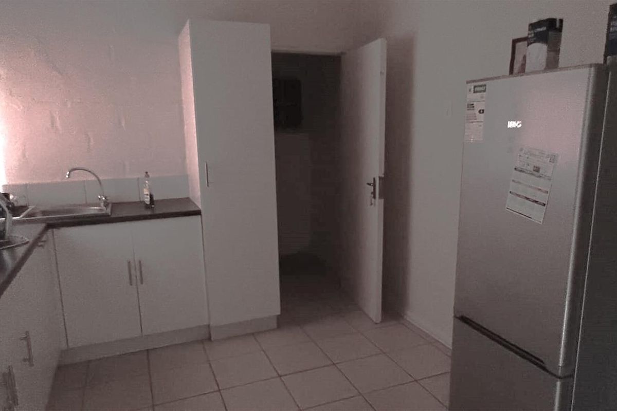 A functional kitchen area featuring white cabinetry, a stainless steel sink, and tiled flooring, providing a practical workspace for industrial or office use.