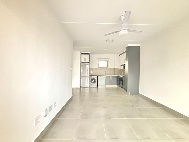Open plan living area featuring a modern kitchen with built-in cabinetry, integrated appliances, and tiled flooring throughout.