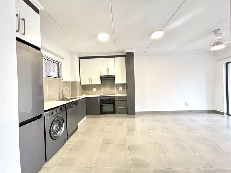 Modern open-plan kitchen featuring two-tone cabinetry, built-in oven, hob, extractor fan, and tiled flooring, seamlessly flowing into the living area.