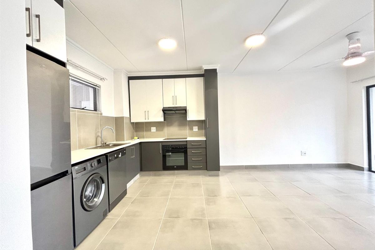 Modern open-plan kitchen featuring two-tone cabinetry, built-in oven, hob, extractor fan, and tiled flooring, seamlessly flowing into the living area.