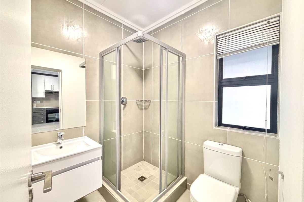 Modern bathroom featuring a corner glass shower enclosure, wall-mounted vanity with basin, and a toilet, finished with neutral floor-to-ceiling wall tiles.