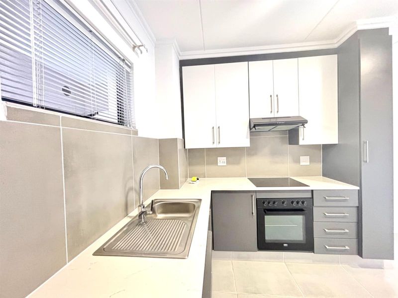 Modern kitchen featuring white and grey cabinetry, integrated oven, electric hob, extractor fan, stainless steel sink, and neutral tiled splashbacks.