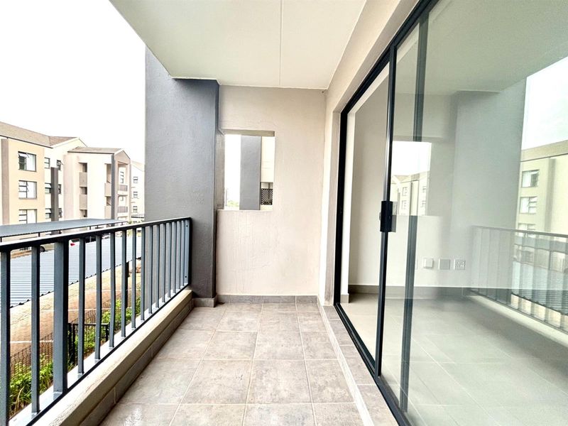 A clean, modern balcony featuring tiled flooring, metal railings, and large sliding glass doors providing seamless access to the interior living space.