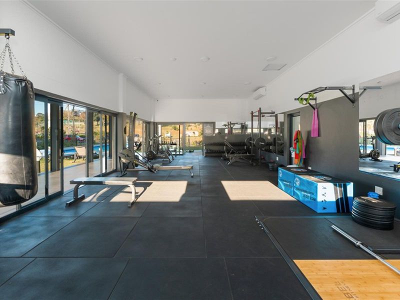 A well-equipped private gym featuring rubber flooring, wall-mounted mirrors, and large sliding glass doors providing natural light and access to the outdoor area.