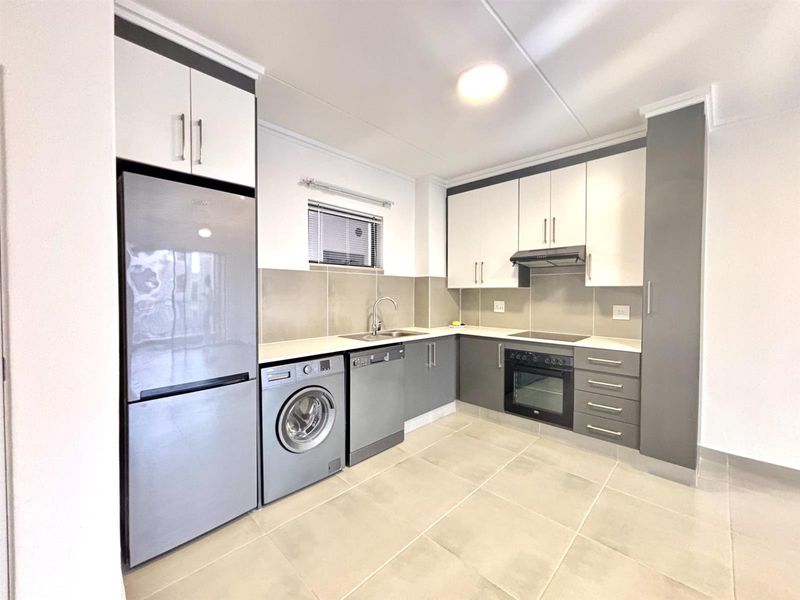 Modern kitchen featuring two-tone cabinetry, tiled backsplash, integrated oven, hob, extractor fan, and dedicated spaces for laundry and dishwasher appliances.