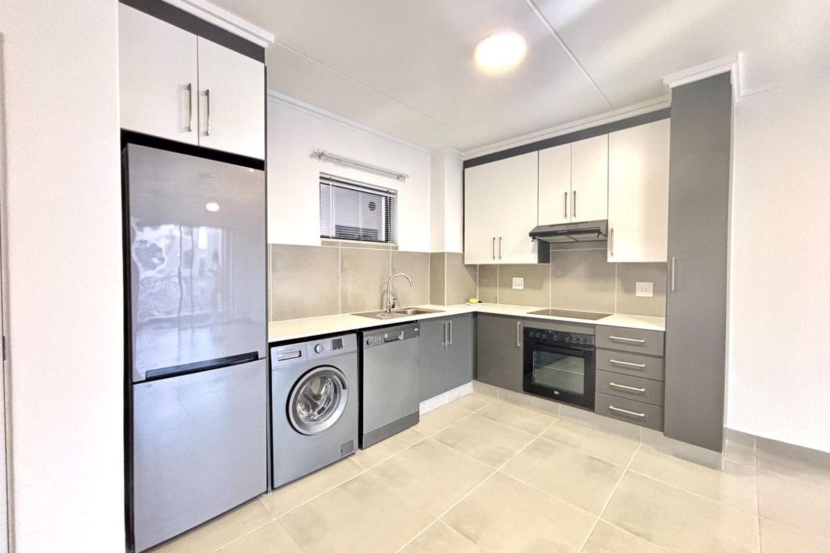 Modern kitchen featuring two-tone cabinetry, tiled backsplash, integrated oven, hob, extractor fan, and dedicated spaces for laundry and dishwasher appliances.