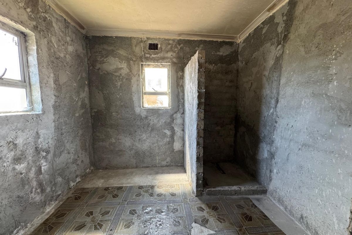 An unfinished bathroom space featuring exposed concrete walls, tiled flooring, and a partial brick partition wall, ready for renovation and final finishes.