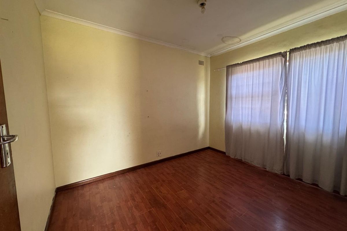 An empty bedroom featuring laminate wood flooring, neutral wall finishes, and a window with curtain tracks.
