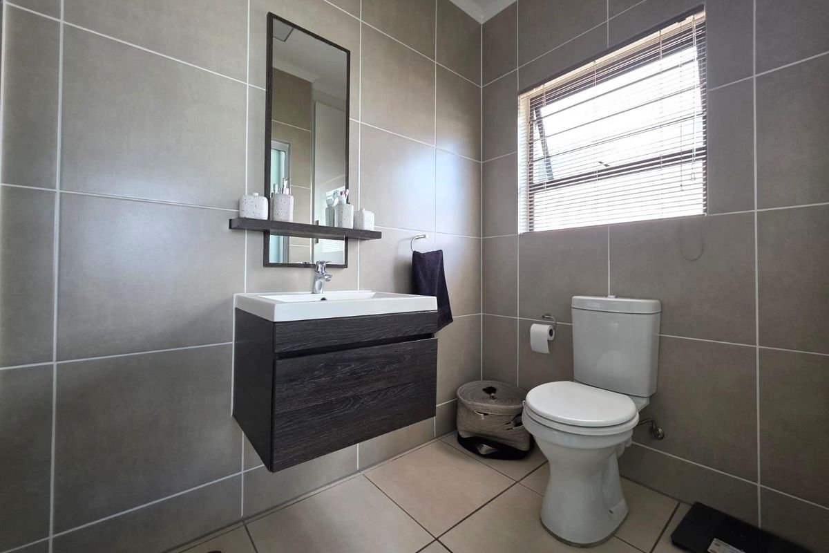 Modern bathroom featuring large format wall tiles, a floating vanity with integrated basin, a wall-mounted mirror, and a toilet.