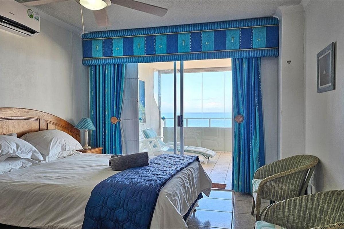 A bedroom featuring a ceiling fan, wall-mounted air conditioning unit, and sliding glass doors leading to a balcony with ocean views.