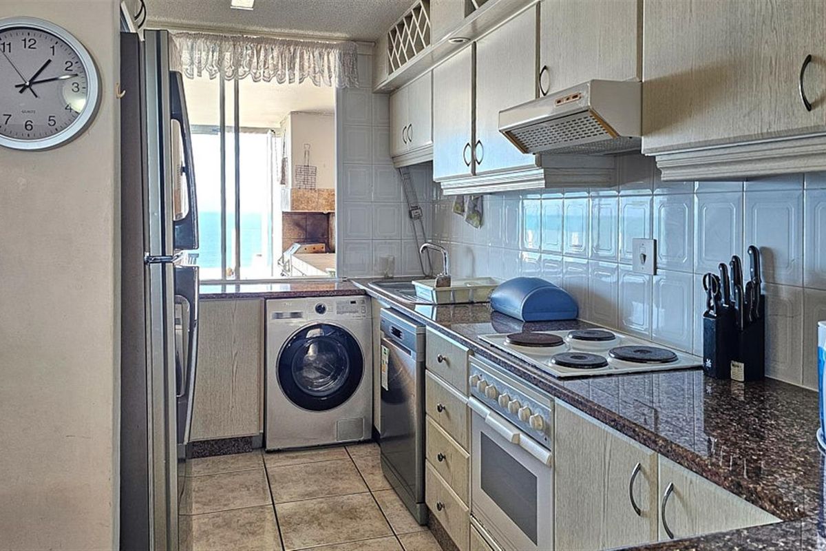 A functional galley-style kitchen featuring granite countertops, built-in oven, electric hob, extractor fan, and integrated laundry appliance space.