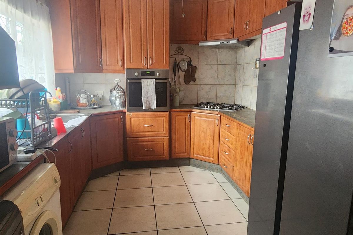 A functional kitchen featuring wood-toned cabinetry, built-in oven, gas hob, extractor fan, and tiled flooring with a practical layout.