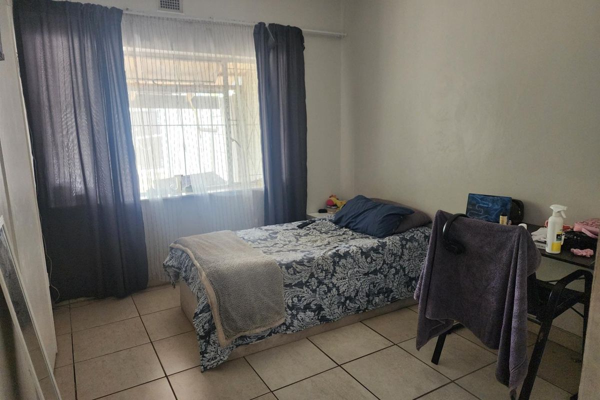 A functional bedroom featuring tiled flooring, a large window with curtain rails, and a ceiling ventilation vent.