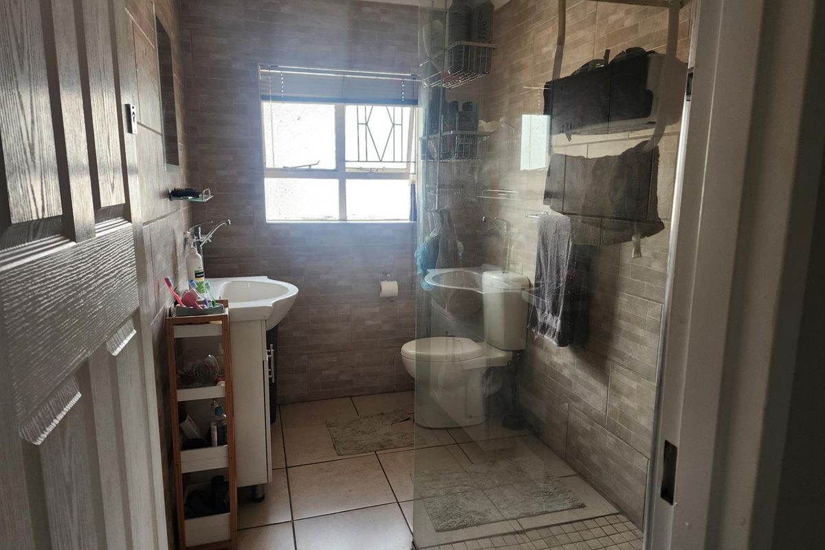 A compact bathroom featuring floor-to-ceiling wall tiles, a glass-enclosed shower, a pedestal basin, and a standard toilet.