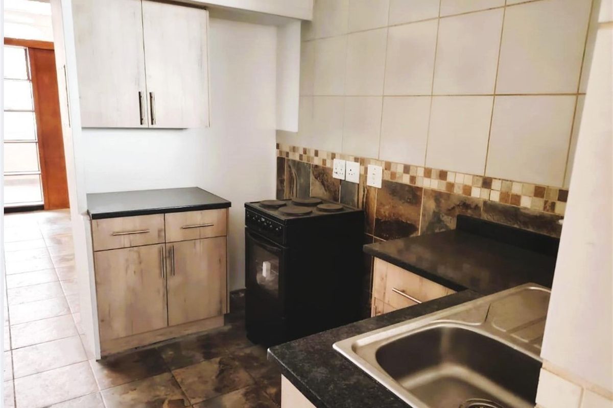 Compact kitchen featuring built-in cabinetry, a dark countertop, a stainless steel sink, and a freestanding stove with a tiled backsplash.