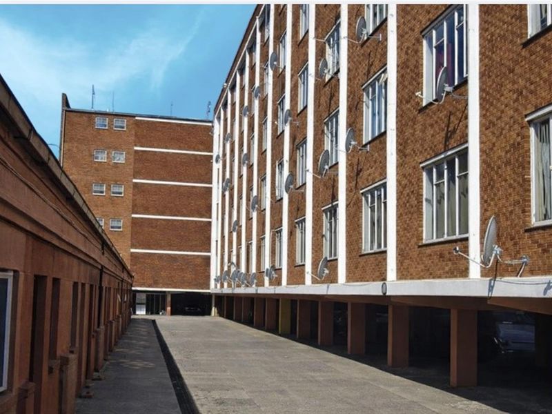 Exterior view of a multi-story apartment building featuring brick facade, concrete support pillars, and multiple satellite dish installations.