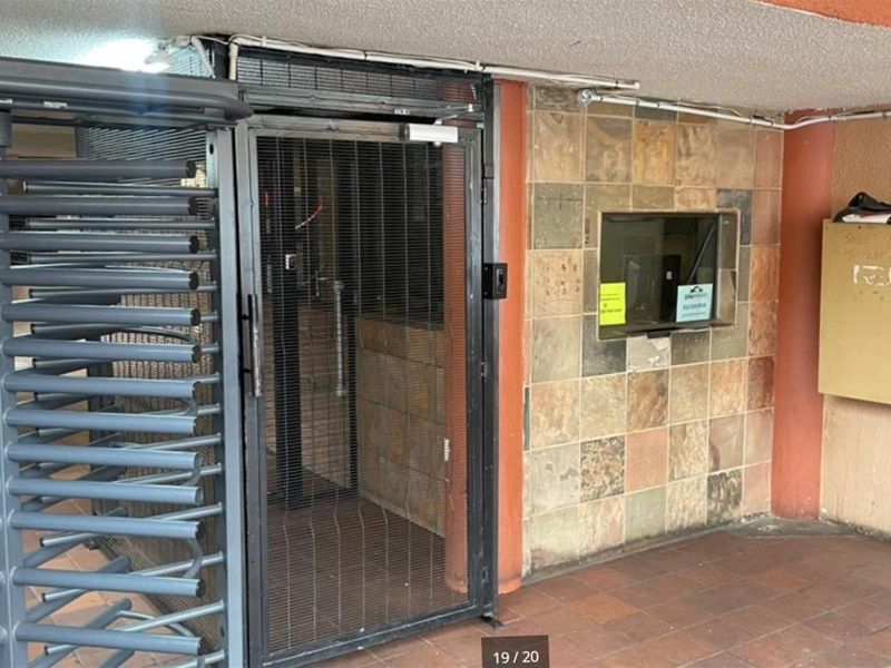 A secure building entrance featuring a metal turnstile, security gate, and tiled wall facade with a service window.