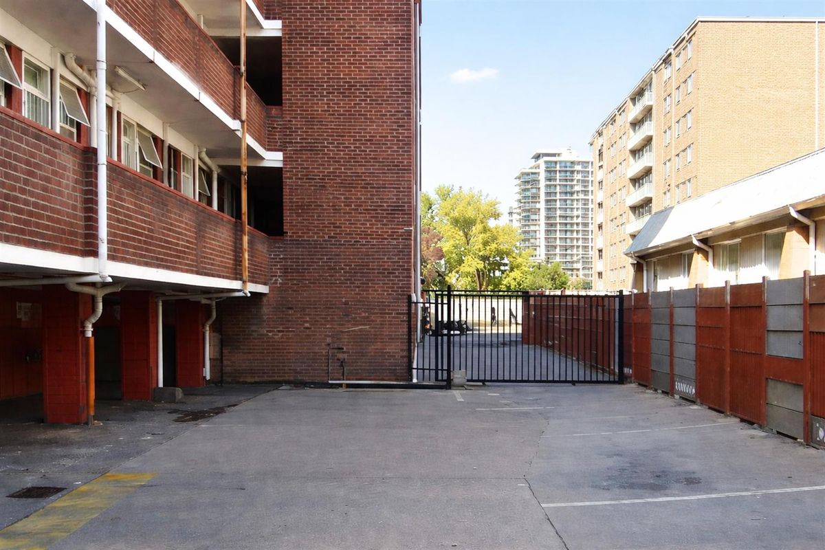 Exterior view of the apartment complex parking area featuring brick facade, paved driveway, and secure metal gate access.