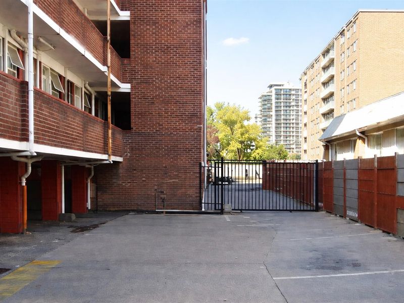 Exterior view of the apartment complex parking area featuring brick facade, paved driveway, and secure metal gate access.