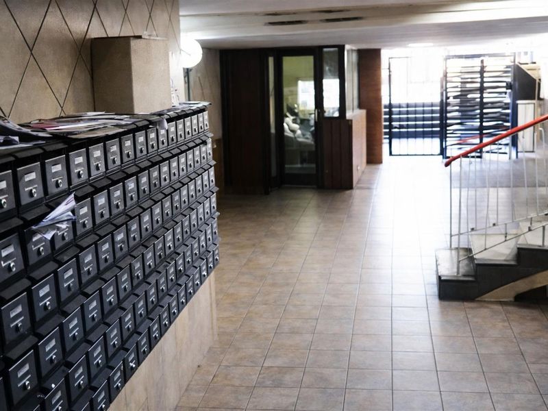 Apartment building entrance lobby featuring a wall of metal mailboxes, tiled flooring, and a staircase with a metal handrail leading to the upper levels.