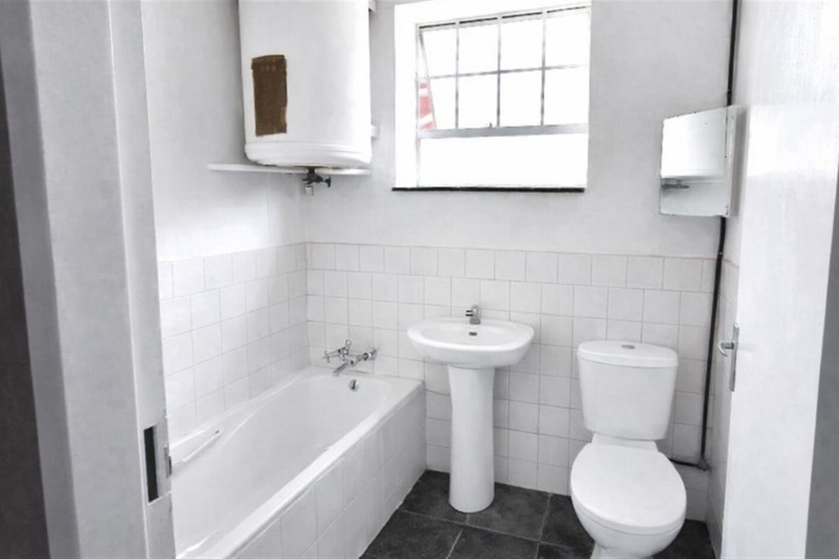 A functional bathroom featuring a white bathtub, pedestal basin, toilet, and an exposed wall-mounted water heater with tiled splashbacks.