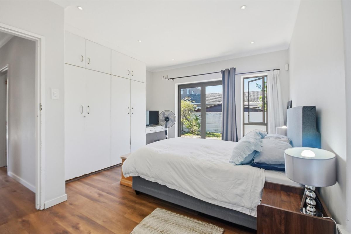 A bright bedroom featuring built-in floor-to-ceiling wardrobes, wood-look flooring, recessed lighting, and direct access to the rear garden through glass sliding doors.