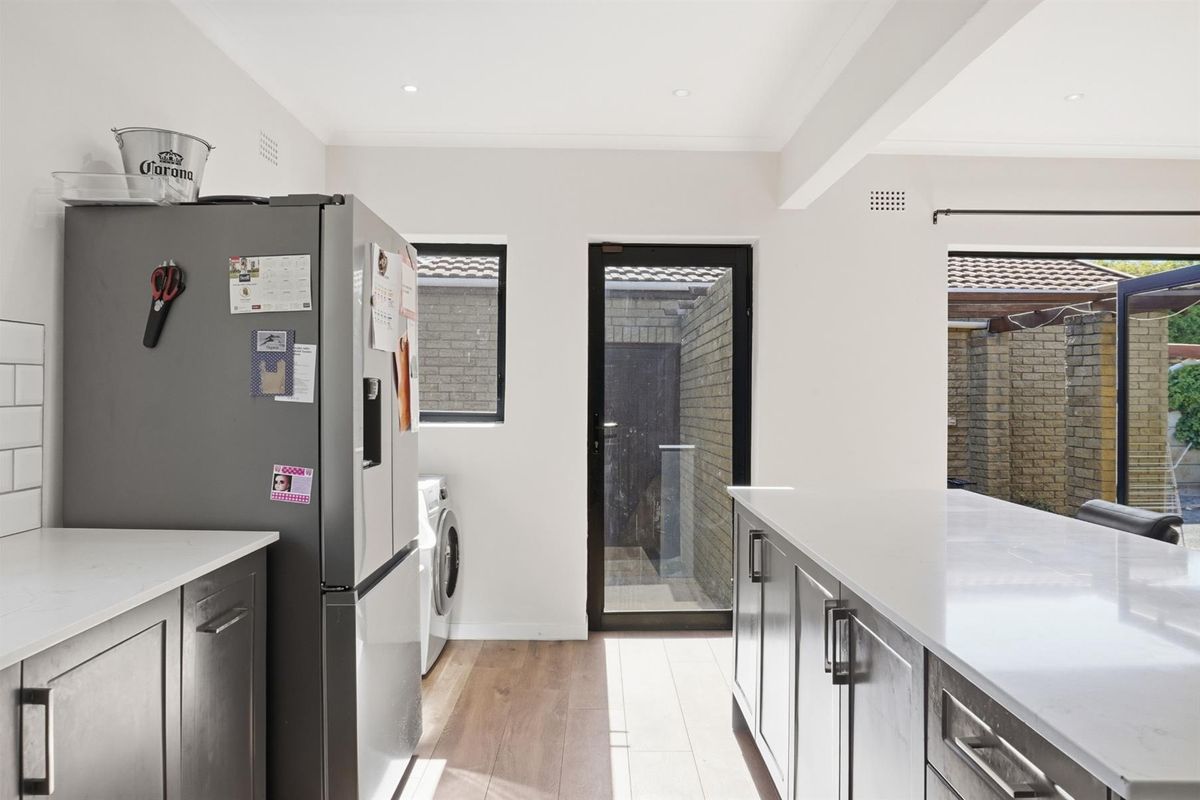 Modern kitchen featuring sleek cabinetry, stone countertops, and a central island, with direct access to an outdoor area through a glass door.