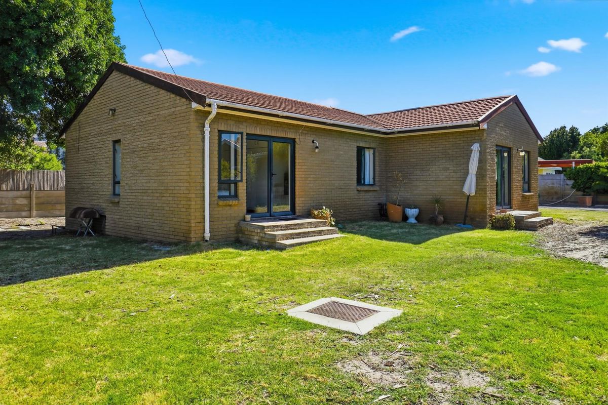 Rear view of a single-story brick house featuring a tiled roof, sliding glass doors, and a spacious backyard area.