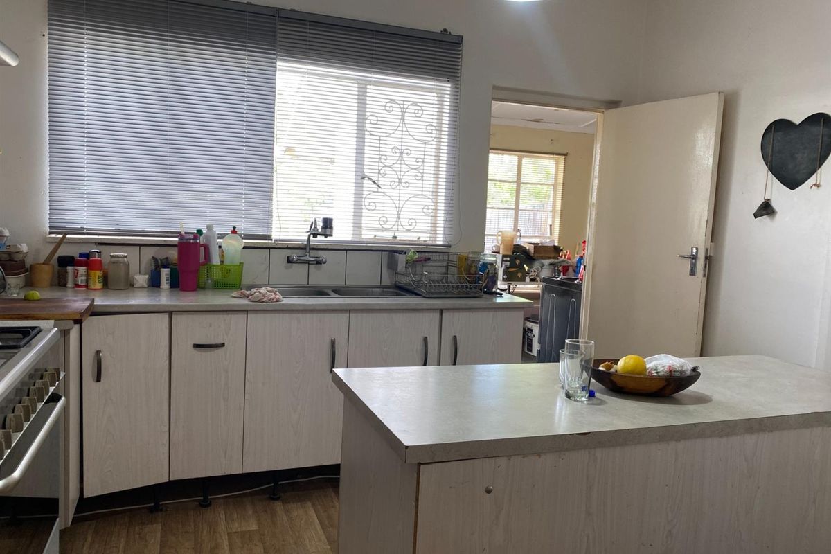Functional kitchen featuring light-toned cabinetry, laminate countertops, double basin sink, and a central island, with a view into an adjacent utility area.