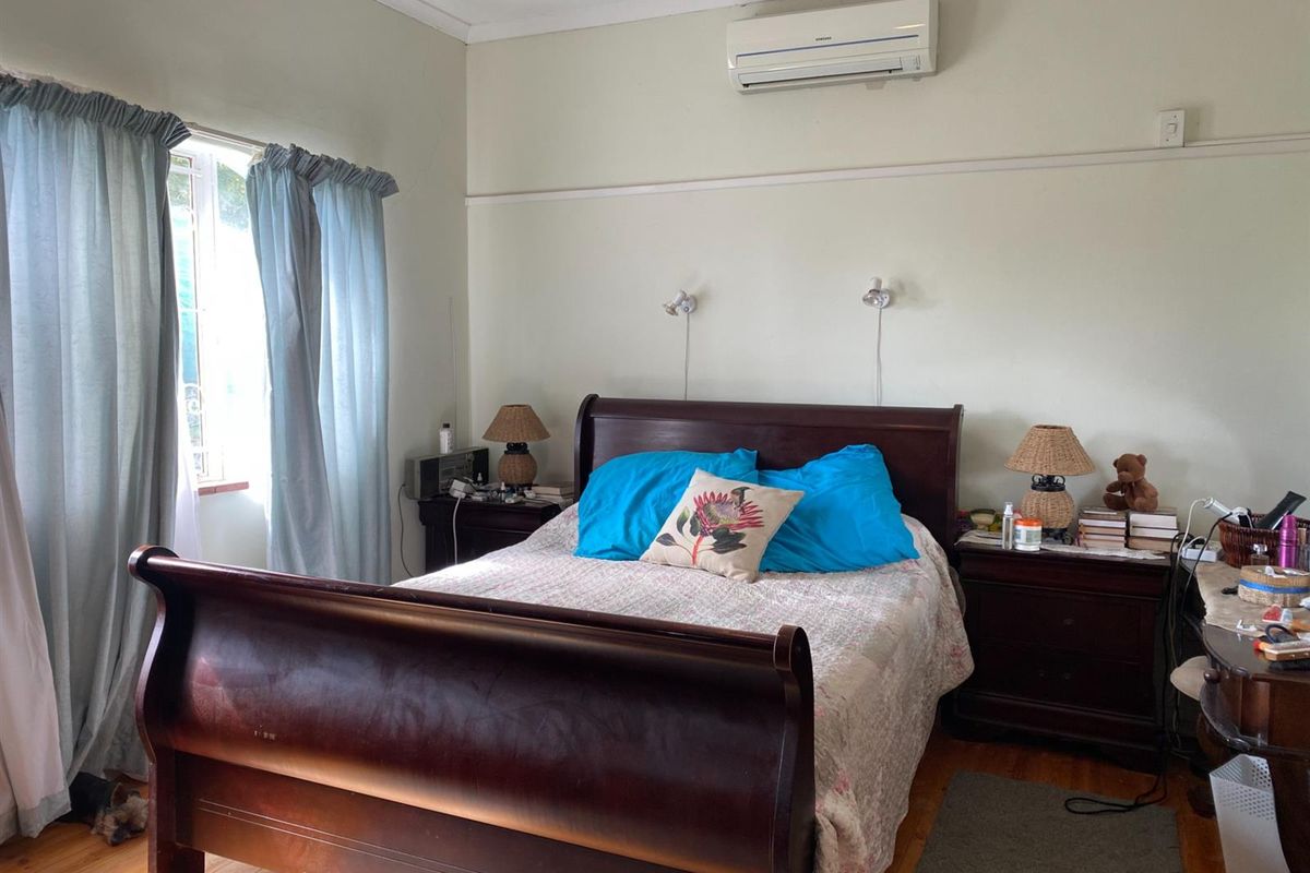 A bedroom featuring timber flooring, wall-mounted air conditioning unit, and dual wall-mounted reading lights.