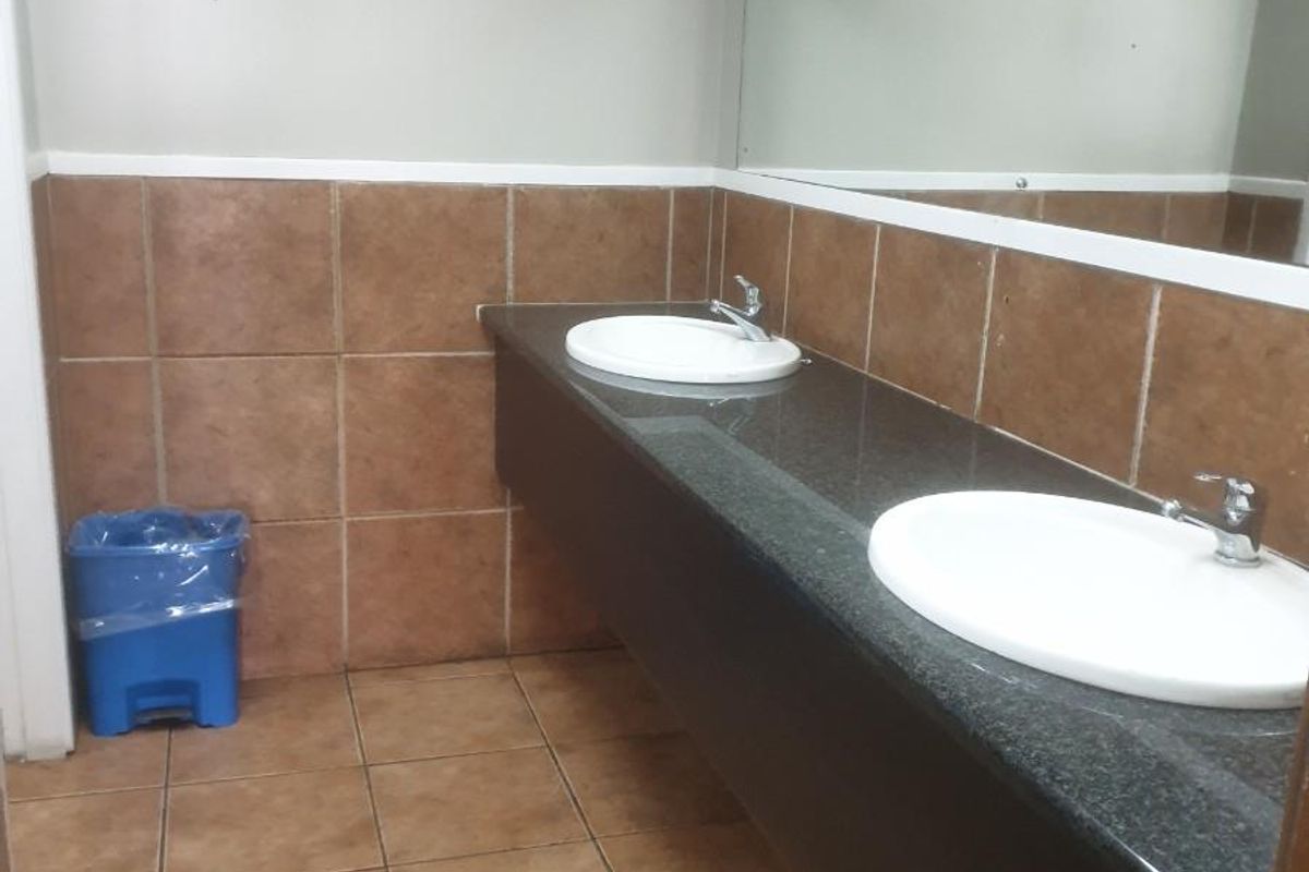 A functional industrial-style bathroom featuring a dual-basin vanity with granite countertop, ceramic wall and floor tiling, and a large wall-mounted mirror.