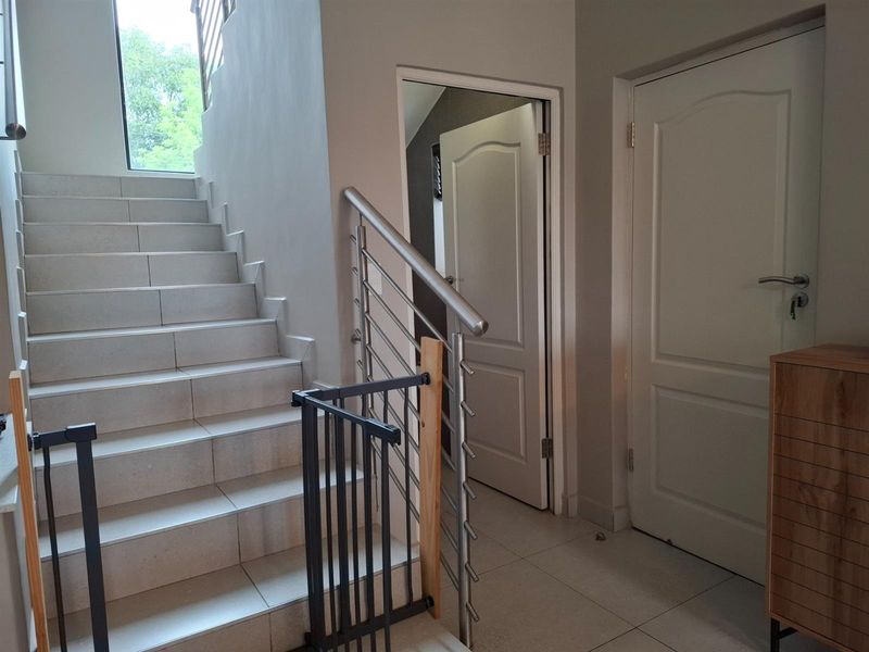 A bright hallway featuring a tiled staircase with a modern stainless steel balustrade and access to adjacent rooms through panelled doors.