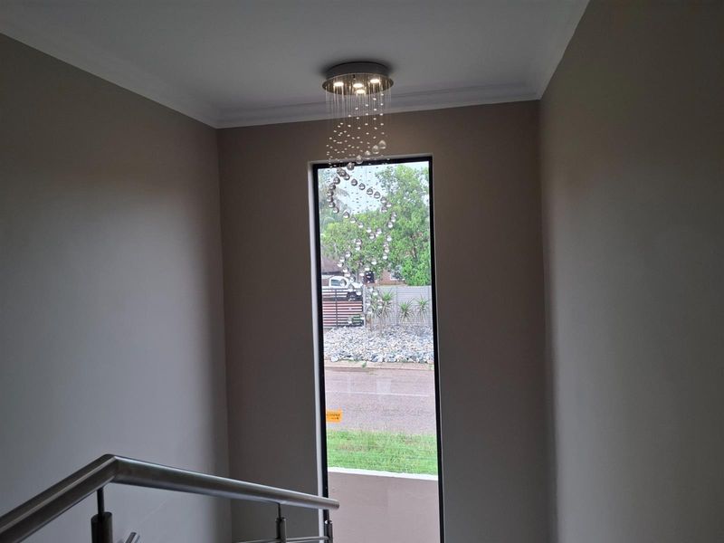 A bright stairwell area featuring a tall vertical window, modern stainless steel handrail, and a decorative crystal pendant light fixture.