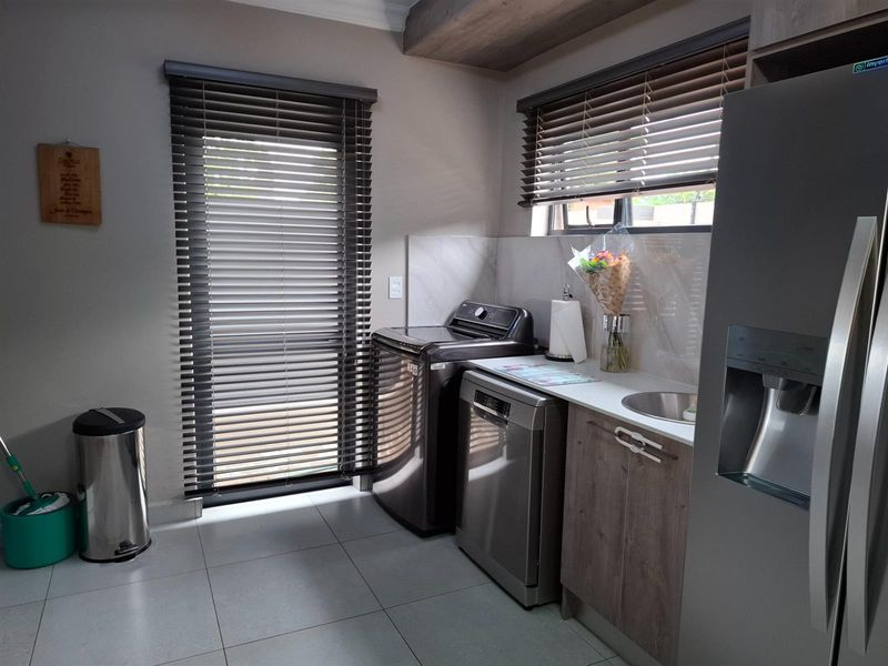 A functional laundry area featuring modern cabinetry, a stainless steel sink, tiled flooring, and venetian blinds.