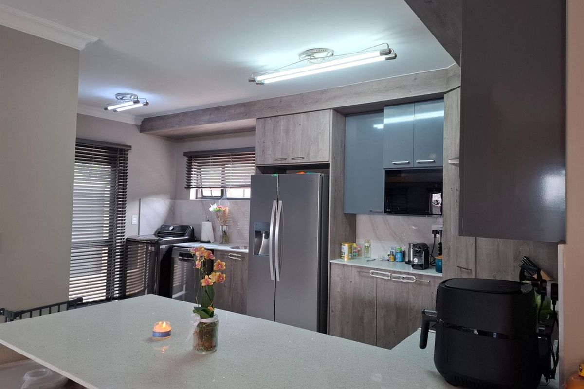 Modern kitchen featuring a stone-topped breakfast island, sleek grey cabinetry, integrated storage, and contemporary lighting fixtures.